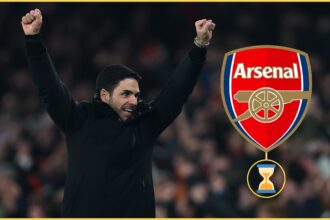Mikel Arteta holds up his arms in celebration next to Arsenal club badge.