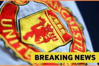 Close-up image of Manchester United logo with yellow breaking news banner