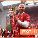Arne Slot holds the Premier League trophy on the pitch at Anfield.