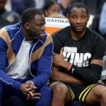 Draymond Green #23 (left) speaks to Jonathan Kuminga #00 of the Golden State Warriors on the bench during their game against the New Orleans Pelicans.